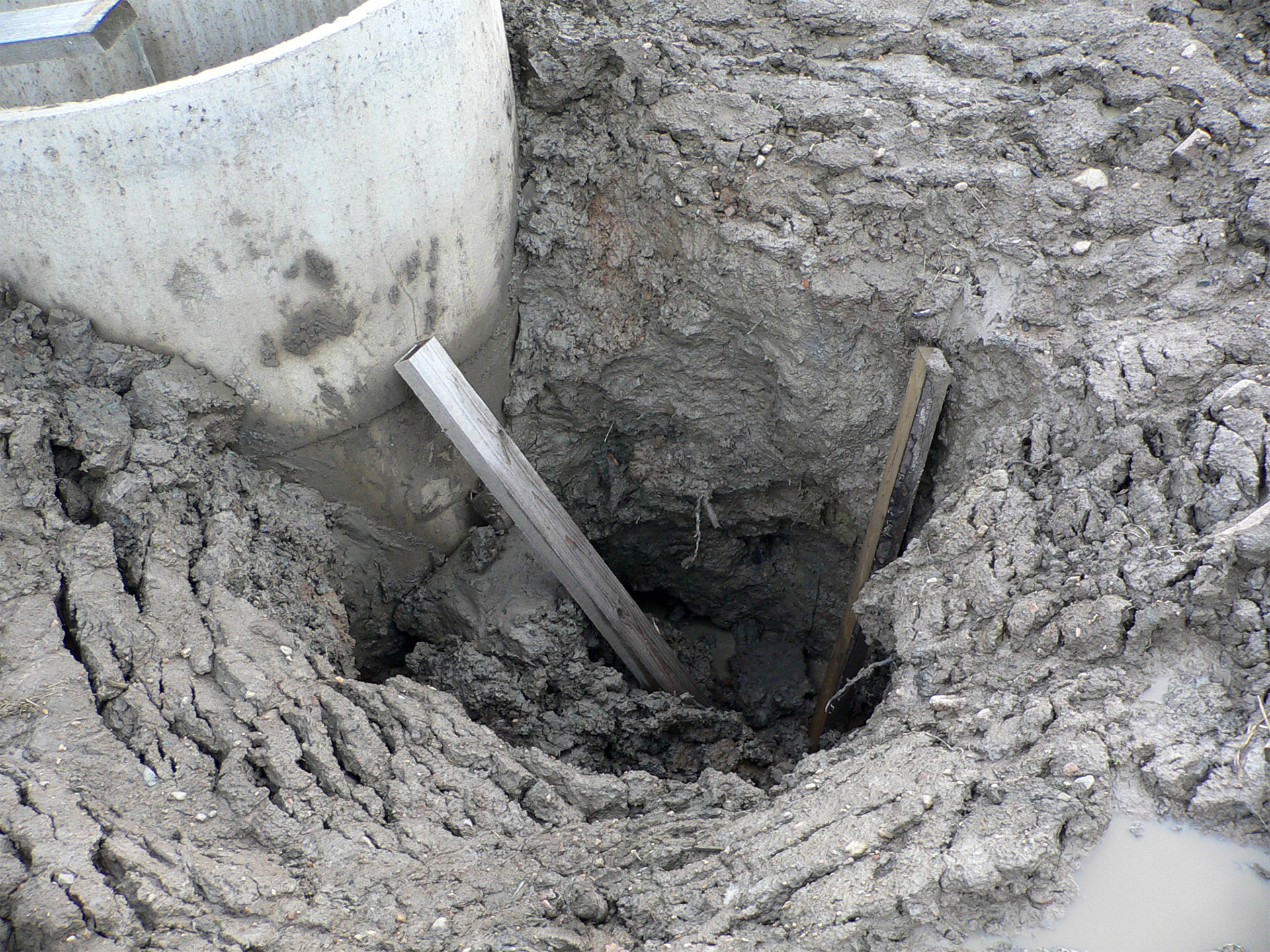 En grop i lerig jord och bredvid syns en betongring.