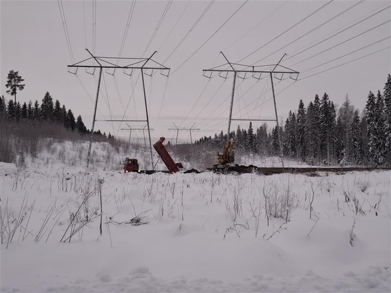 Talvinen maisema, jossa voimalinjoja ja työkoneita.